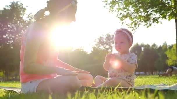 夏の緑の芝生の上に彼女の母親と一緒に座っている小さな女の赤ちゃん スローモーション 120 Fps 幸せな子供時代と親の概念 — ストック動画