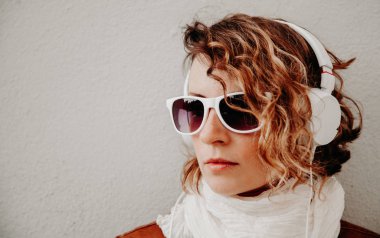 Güzel genç kadın bir güneş gözlüğü ve müzik ayakta duvara dinlerken kulaklık. Rahat tarzı kavramı