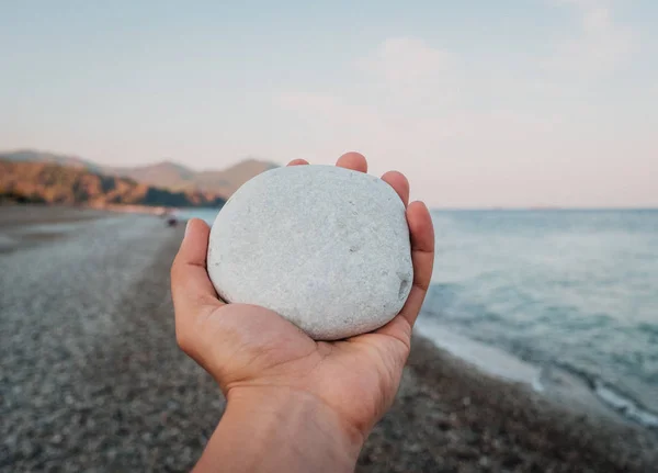 Pietra bianca di ghiaia in mano su sfondo paesaggio incredibile in spiaggia. Concetto viaggio e vacanza — Foto Stock