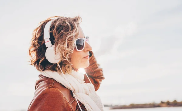 Mujer joven con auriculares blancos escuchando música brillante fondo del cielo en el día de verano —  Fotos de Stock