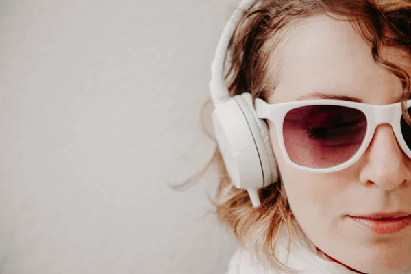 Hermosa joven con gafas de sol y auriculares escuchando música de pie en la pared. Concepto de estilo casual — Foto de Stock