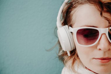 Güzel genç kadın bir güneş gözlüğü ve müzik ayakta duvara dinlerken kulaklık. Rahat tarzı kavramı