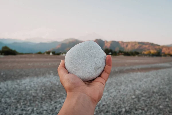 Λευκό βότσαλο πέτρα στο χέρι στο εκπληκτικό τοπίο φόντου στην παραλία. Ταξίδια και διακοπές έννοια — Φωτογραφία Αρχείου