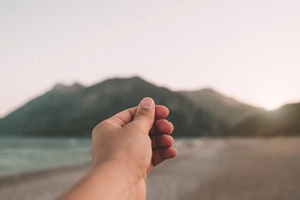 Una mano simula la celebración de una foto, postal o nota en la hermosa puesta de sol sobre las montañas en la playa en el día de verano . — Foto de Stock