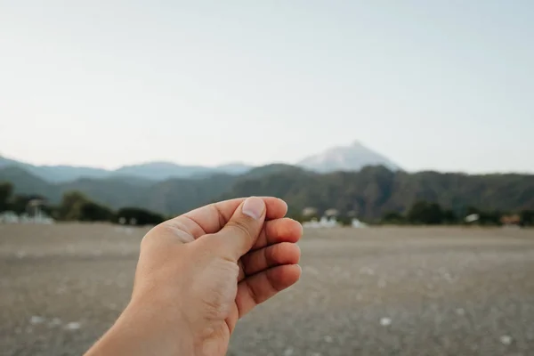 Bir fotoğraf, kartpostal veya Not üzerinde güzel gün batımı plajda Dağların üzerinden yaz günü içinde tutan bir el simüle. — Stok fotoğraf