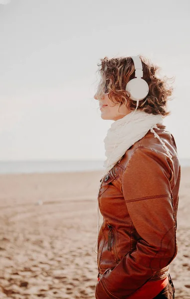 Mujer joven con auriculares blancos escuchando música en la playa en el día de verano —  Fotos de Stock