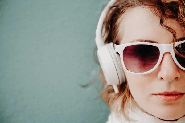 Mulher bonita em óculos de sol e fones de ouvido ouvindo música em pé na parede. Conceito de estilo casual — Fotografia de Stock