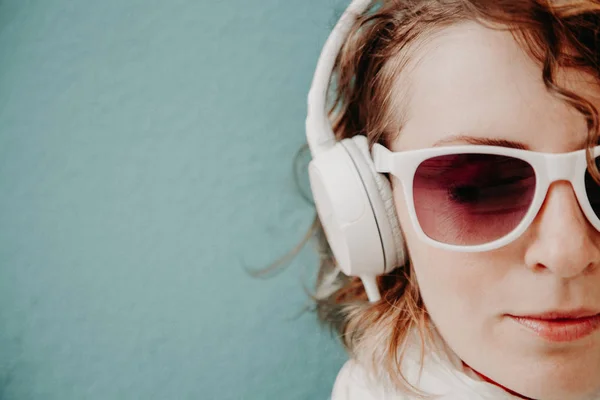 Hermosa joven con gafas de sol y auriculares escuchando música de pie en la pared. Concepto de estilo casual — Foto de Stock