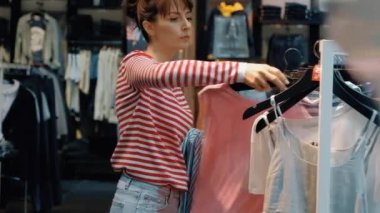Bir denim mağazasında genç güzel kadın satıcı askıları üzerinde giysi asılı