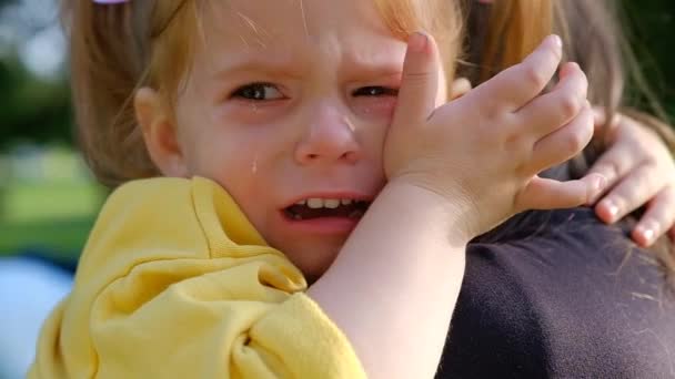 Nahaufnahme Porträt eines kleinen charmanten Mädchens, das in den Armen seiner Mutter weint — Stockvideo
