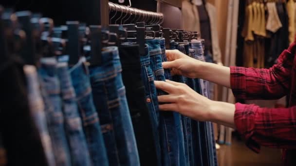 Seitenansicht einer jungen hübschen Frau in Freizeitkleidung wählt Jeans — Stockvideo