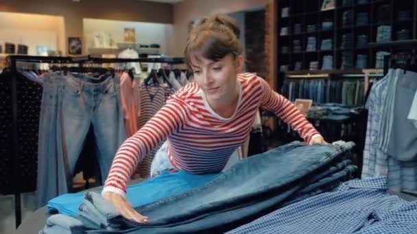 Mulher bonita em roupas casuais é alisar jeans deitado em uma pilha — Vídeo de Stock