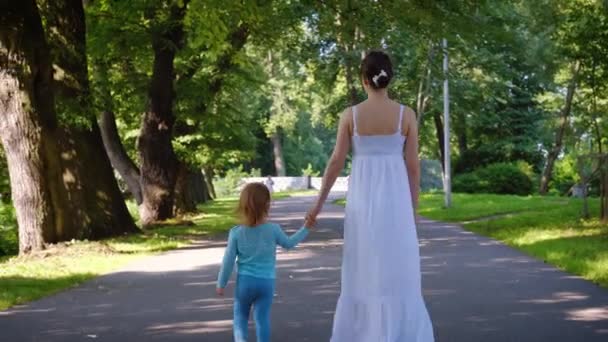 Bakifrån av en ung mor i långa vita sundress promenader med charmig dotter — Stockvideo