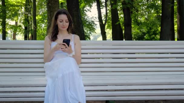 Mooie jonge vrouw is het typen van een bericht in een smartphone — Stockvideo