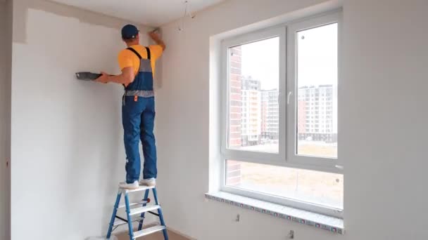 Male worker in a special suit paints the walls in the room in white — Stock Video