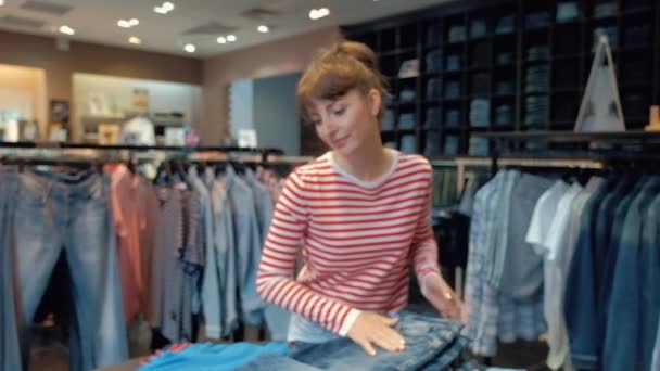 Krásná mladá žena v neformálním oblečení je vyhlazování džínů, které leží na hromadě — Stock video