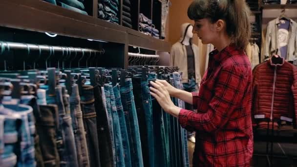 Вид сбоку молодой красивой женщины в повседневной одежде выбирает джинсы — стоковое видео