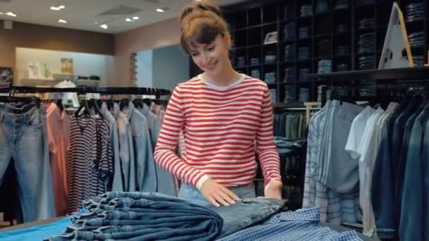 Šťastná mladá žena prodávajících v džínové Boutique prolistování přes hromádku džínů — Stock video