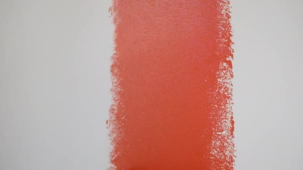 Closeup hand of a builder paints a white wall with red paint using a roller — Stock Video