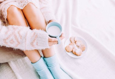 Elinde bir fincan sütle yatakta yatan genç bir kadın evde kalmaktan zevk alıyor..