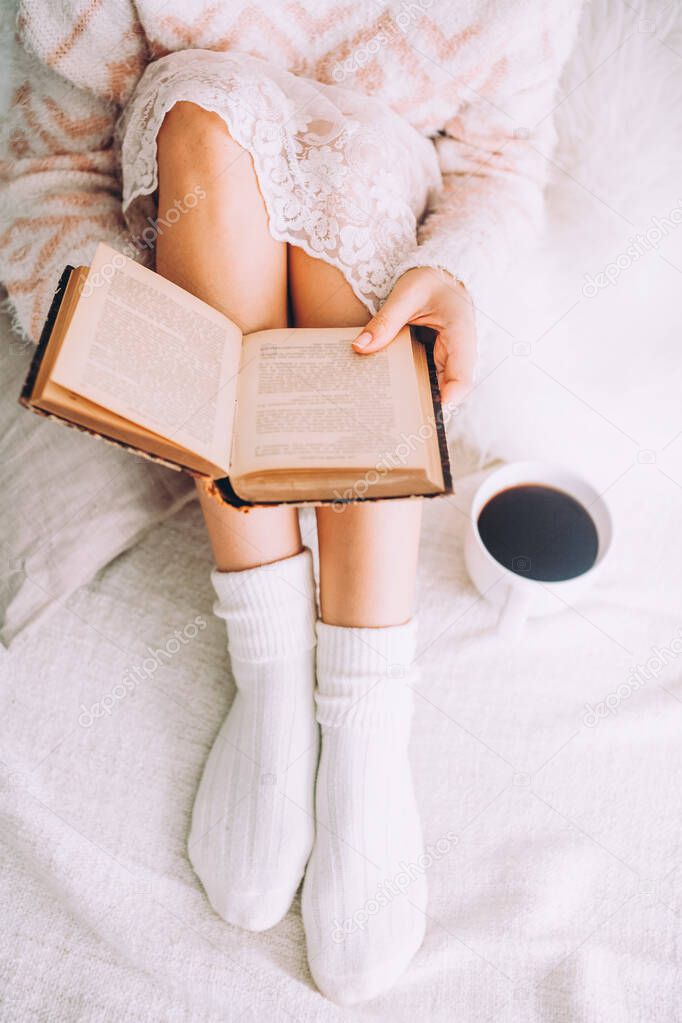 Young woman on the bed with old book and cup of coffee enjoys her stay.
