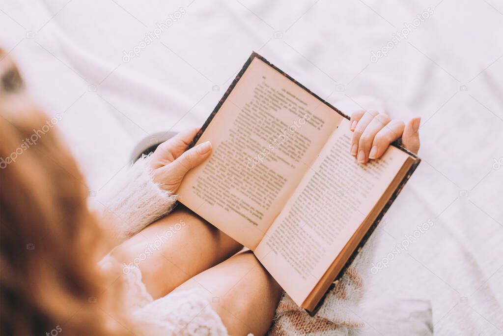 Young woman on the bed with old book and cup of coffee enjoys her stay.
