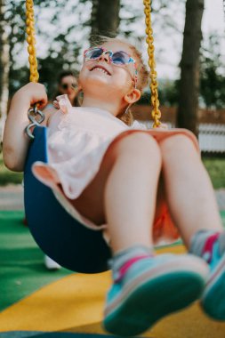 Mutlu Gülen Çocuk yaz parkında salıncakta sallanıyor. Güneş gözlüklü kız eğleniyor. Klasik film görüntüsü