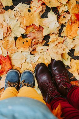 Anne ve çocuk ayaklarının sonbahar yaprakları üzerinde duran deri ayakkabılarının en üst görüntüsü. Doğada yürümek. Klasik film görüntüsü