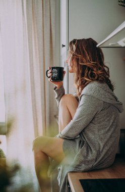 Genç ve güzel bir kadın evdeki mutfağında oturup kahve içiyor ve pencereden dışarı bakıyor. Sabahın tadını çıkarıyor. Klasik film görüntüsü