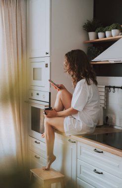 Genç ve güzel bir kadın evdeki mutfağında oturup kahve içiyor ve akıllı telefonlardan keyif alıyor. Gülümseyen kadın telefon mesajı okuyor. Klasik film görüntüsü