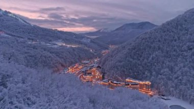 Hava dron beyaz kış Rosa Khutor tatil Soçi görüntüsünü oluşturma. Ağaçlar kar kaplı. Akşam aydınlatma. Güneş battıktan sonra. Kar orman yukarıda uçan düşük