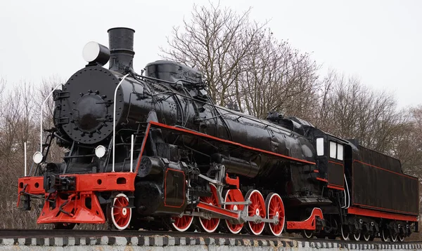 Front side view of old classic black steam locomotive with red decoration on railroad track