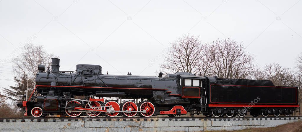 Side view of old classic black steam locomotive with red decoration on railroad track