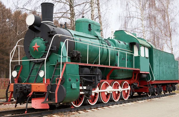 Side view of classic old green soviet steam locomotive with red star on rail tracks