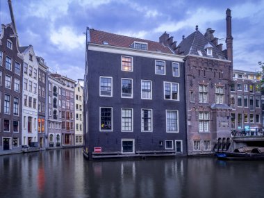 Amsterdam, Hollanda - 18 Temmuz 2018: Geleneksel kanal Amsterdam'da gece karanlığında evler. Kanaldaki binalar şimdi çok popüler olan geleneksel Hollanda mimari biçimidir.