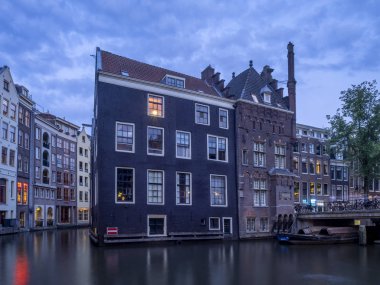 Amsterdam, Hollanda - 18 Temmuz 2018: Geleneksel kanal Amsterdam'da gece karanlığında evler. Kanaldaki binalar şimdi çok popüler olan geleneksel Hollanda mimari biçimidir.