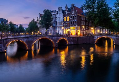Alacakaranlıkta, Kanal, köprü ve ortaçağ evleriyle Amterdam şehir manzarası aydınlandı. Amsterdam, Hollanda