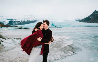 Iceland Wedding. Lovely couple hugs in Glacier Lagoon in cold windy day clipart