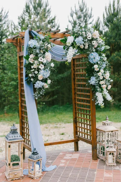 Floral arch with blue cloth and wooden elements at a rustic  wedding ceremony
