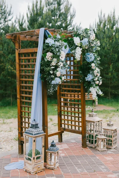 Floral arch with blue cloth and wooden elements at a rustic  wedding ceremony