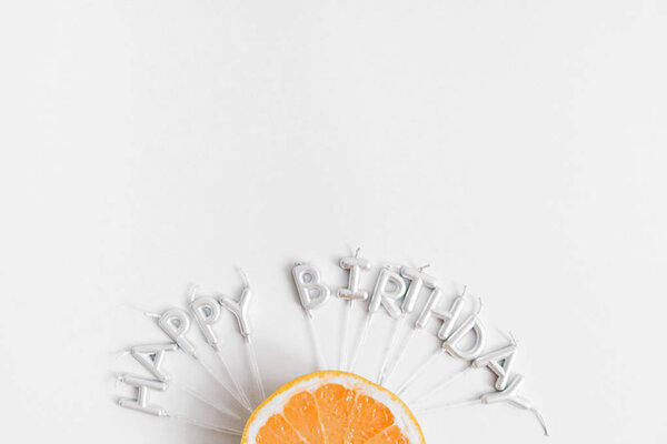 Half of orange on white background and candles with words Happy Birthday. Flat lat, top view. copy space