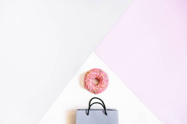 Kağıt torba ve gri ve pembe pastel arka plan üzerinde pembe bir çörek. Flatlay, üstten görünüm alanı kopyalayın. Alışveriş kavramı