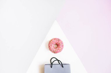 Kağıt torba ve gri ve pembe pastel arka plan üzerinde pembe bir çörek. Flatlay, üstten görünüm alanı kopyalayın. Alışveriş kavramı