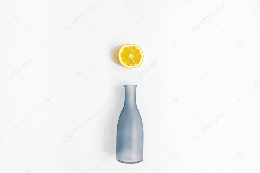 Water bottle and a half of lemon on white background. Flat lay, top view