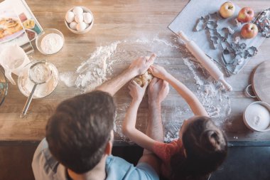 Overhead view of father and daughter kneading dough together clipart