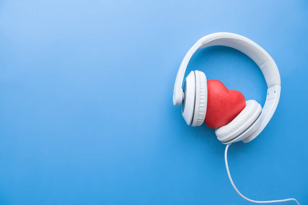 top view of wired headphones with red heart sign in middle on blue surface
