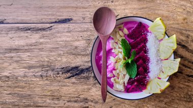 Pitaya smoothie kahvaltı kase ejderha meyve, nane, badem gevreği, chia tohumu, ananas ile tepesinde. Peçete ve kaşıkla besleyici yaz yemeği. ahşap arka plan üzerinde