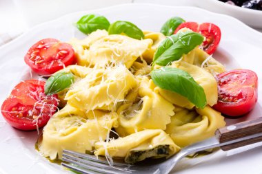 Ravioli ıspanak doldurma, rendelenmiş peynir ve beyaz tabakta kokteyl domates ile