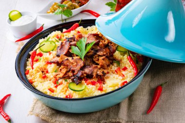 Beyaz arka planda kuskus, sebze ve etli Tajin.