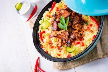 Beyaz arka planda kuskus, sebze ve etli Tajin.